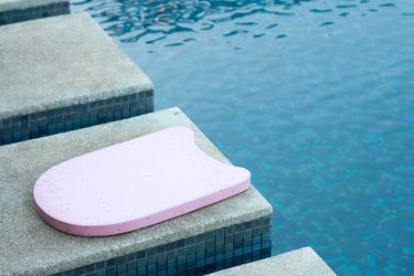 Pink kickboard by the side of a pool to help people become better swimmers