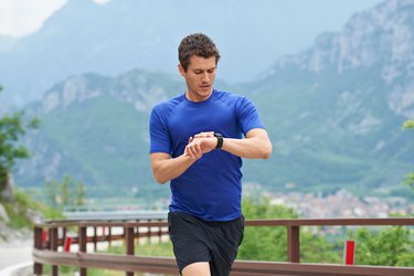 Man running outside in the mountains looking at running watch.