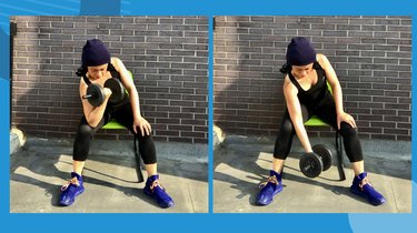 woman performing seated concentration curl dumbbell exercise outside in front of brick wall