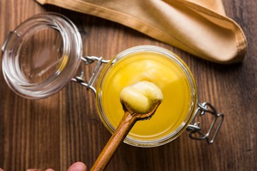 Ghee, or clarified butter, in glass or copper container or ceramic jar with spoon, selective focus
