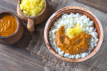 an Indian dish, ghee and butter chicken sauce on rice on a wooden table