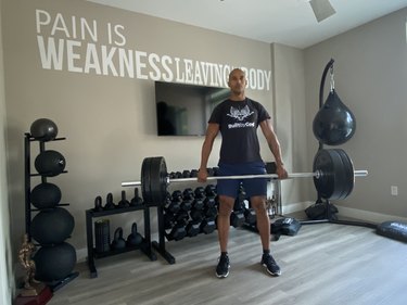 Man doing a deadlift with barbell in home gym during a superset workout with burpees