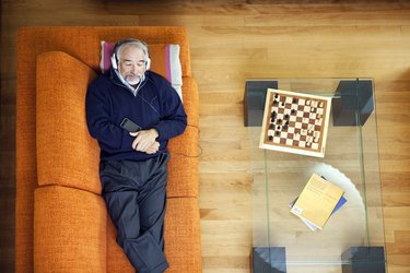 Older man resting on orange couch and listening to music during colonoscopy recovery