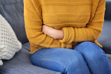 Woman sitting on a couch experiencing bloating after colonoscopy