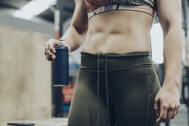 close up of woman's midsection at gym holding a blue canned drink