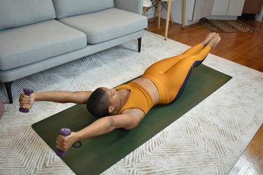 Woman doing a cardio Pilates workout in her living room with hand weights