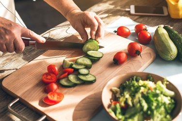 Las manos de un hombre cortando verduras frescas, como las que se comen en la dieta Noom