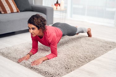 Woman holding a plank in her living room during a Pilates workout for beginners