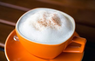 A pumpkin spice latte served in an orange mug, with milk foam and pumpkin pie spice on top