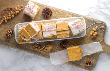 A plate of orange pumpkin pie fudge on a wooden cutting board, surrounded by pinecones