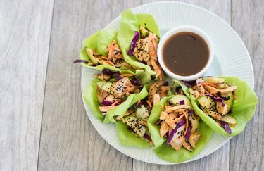 A plate of lettuce cups with kimchi and grilled chicken, and a dipping sauce on the side