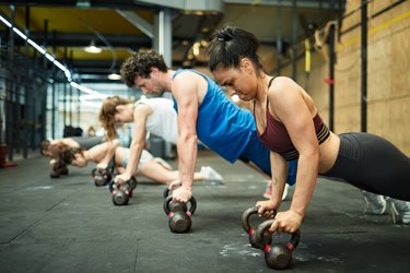 Group of hispanic people doing planks with kettlebells at the gym.