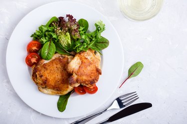 Roast chicken  legs on white plate over light gray plaster texture table