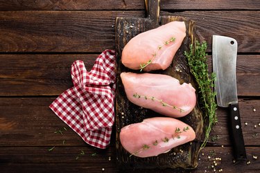 Raw chicken breasts fillets with thyme and spices on wooden cutting board on rustic background, copy space, directly above