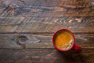 Red mug with freshly brewed coffee with appetizing crema on aged wood kitchen table. Cozy winter fall holiday atmosphere copy space