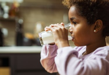 profile of a child with pierced ears wearing a purple top and drinking a glass of milk, wondering if dairy is bad for congestion