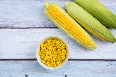Organic corncob on wood, maize in bowl