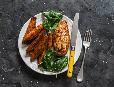 Baked chicken breast with sweet potatoes and spinach on a dark background, top view. Balanced healthy lunch