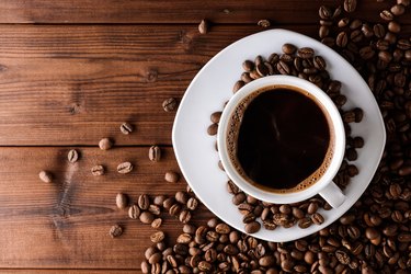 Coffee cup with saucer and beans on wooden table.