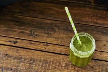 Wheat grass juice in a mason jar on a rustic aged wood table top.