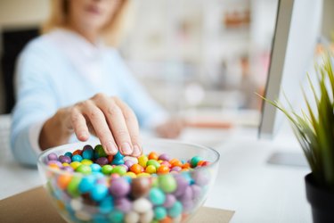 Close-up of unrecognizable businesswoman sitting at table and eating sweet beans while working in office