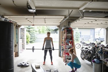 Young women friends working out, weightlifting in garage