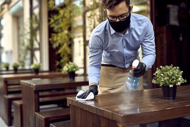 photo of restaurant server wearing face mask and sanitizing wooden table outside