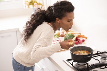 Woman cooking, blowing a spoonful of hot soup.