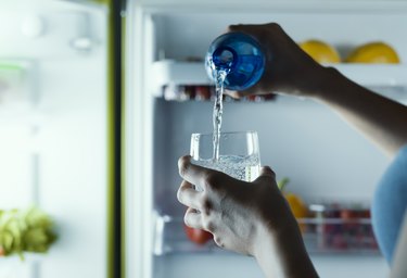 Woman taking a bottle of water from the fridge and pouring it into a glass while wondering, "How long to break coffee addiction?"