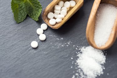 Wooden spoons containing stevia and sugar on a gray background.