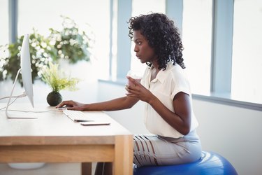 woman working at a desk and using an exercise ball as a desk chair