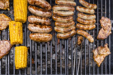 Different meat, maize and fried sausages on barbecue grill