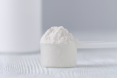 a scoop with white powder closeup and a jar on gray background