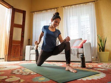 Woman stretching her hips on mat in living room for joint mobility