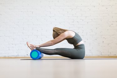 Attractive woman doing typical stretching, head to knees with foam blue roller, paschimottanasana pose, indoor at club