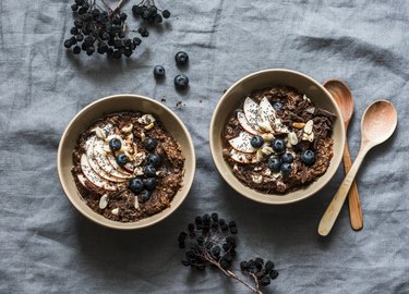 Chocolate oatmeal with apples and blueberries - healthy vegetarian breakfast on a grey background, top view. Flat lay, copy space