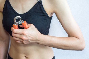 Cropped shot view of woman handle a hand grip for exercise with white wall background.