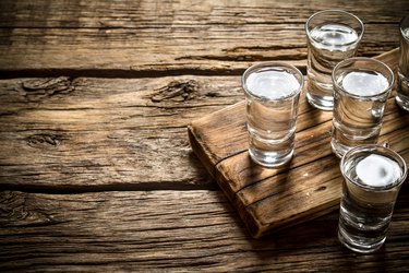 four shot glasses with vodka on a wooden board