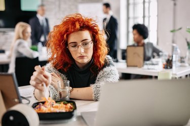 A sad woman eating salad at her desk at work
