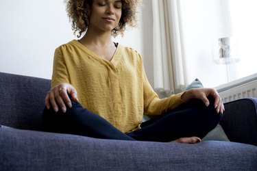 Young woman sitting on couch at home meditating