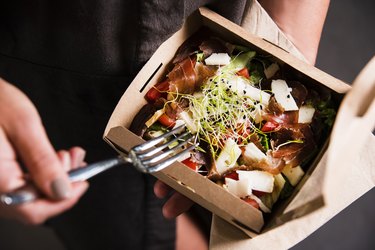 Woman's hand is holding a take away fresh salad in a lunch box.