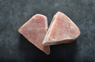 Two frozen tuna fish steaks on dark backgound shot from above