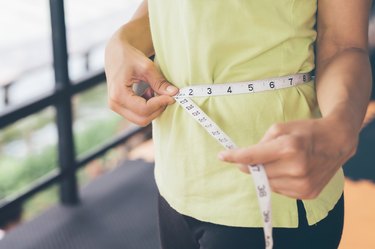 A woman measuring her waist size with a tape measure