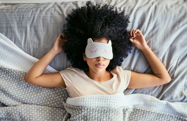 A woman sleeping on her back in bed and wearing an eye mask
