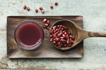 Glass of pomegranate juice and wooden spoon with pomegranate seed on wooden tray