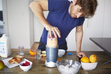 Man making smoothie in blender while standing in kitchen