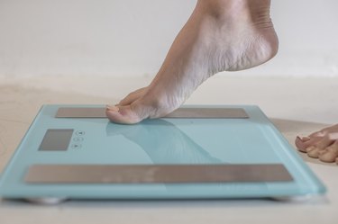 Young woman stepping onto weighing scales, close up of foot