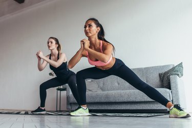 Two fit girls doing home workout performing lateral lunges at home