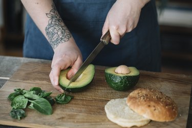 Woman preparing vegan burger, slicing avocado