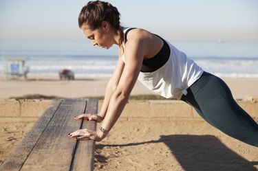 Side view of woman doing push-ups on Bench at beach